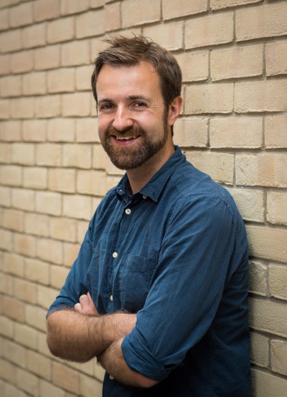 author standing against a wall with his hands folded over his chest