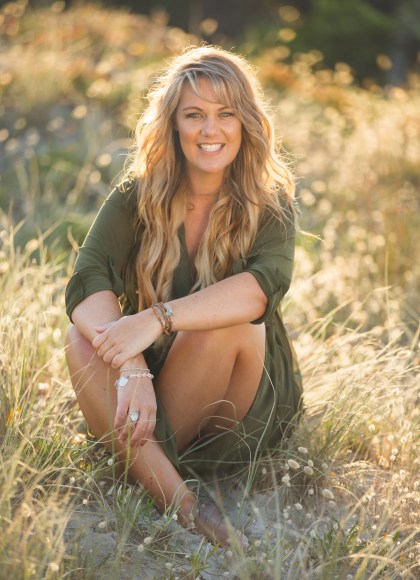 Photo of author Emma Mildon sitting in a field of grass and smiling at the camera